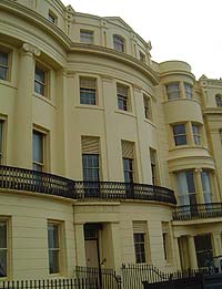 Shows a photograph of the Regency Townhouse. It is a four-storey building painted cream. The first floor has a balcony and columns, ornate mouldings and window blinds decorate the fascia.